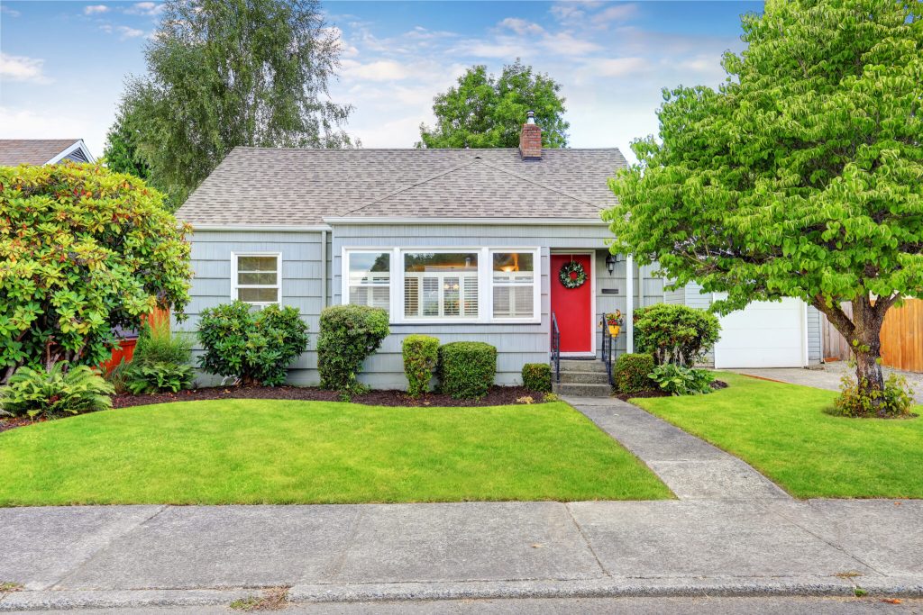 Cozy home exterior with a red door, surrounded by green shrubs and a well-maintained lawn, reflecting a welcoming atmosphere for winter warmth and community living in Grantsburg.