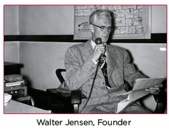 Walter Jensen, founder of Jensen-Sundquist Insurance Agency, seated at a desk with a microphone and papers, reflecting the agency's historical roots in northwest Wisconsin.