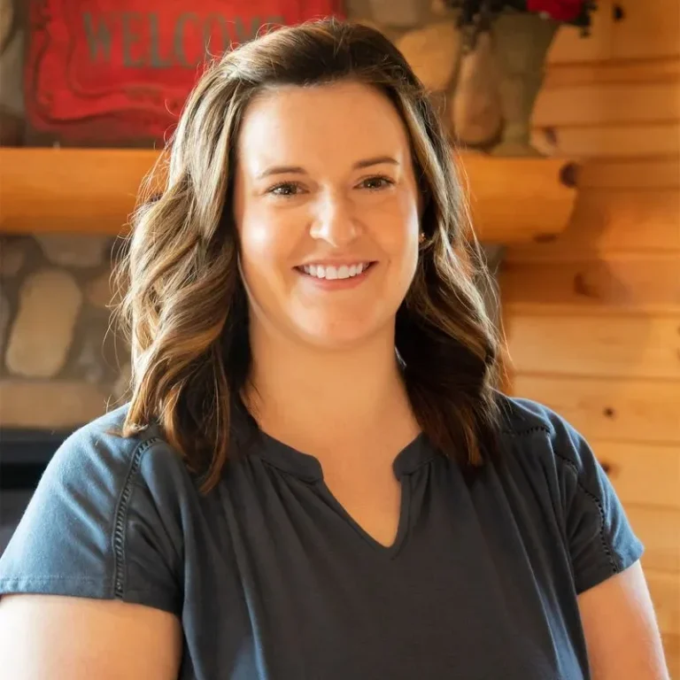 Dessie Thoreen, Personal Lines Agent at Jensen-Sundquist Insurance Agency, smiling in a casual setting with a welcoming wooden backdrop.