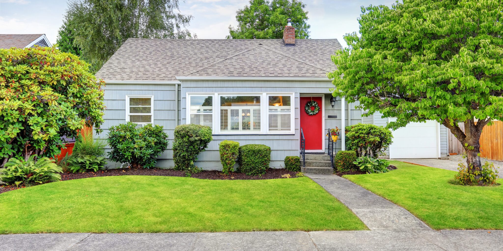 Charming single-story home in Grantsburg with a red front door, surrounded by lush greenery and well-maintained landscaping, symbolizing the importance of homeowners insurance for property protection.