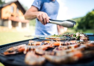 Unrecognizable man cooking seafood on a barbecue grill in the backyard on a sunny day.