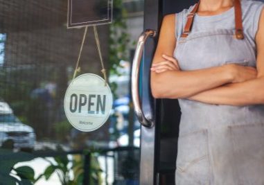 The woman is a waitress in an apron, the owner of the cafe stands at the door with a sign Open waiting for customers. Small business concept, cafes and restaurants
