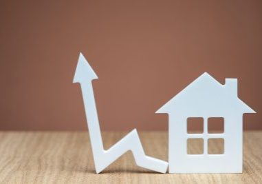 An increase in the interest rate for a mortgage or an increase in the cost of insurance for a property. White house model and graphic arrow pointing up close up on brown background. copy space